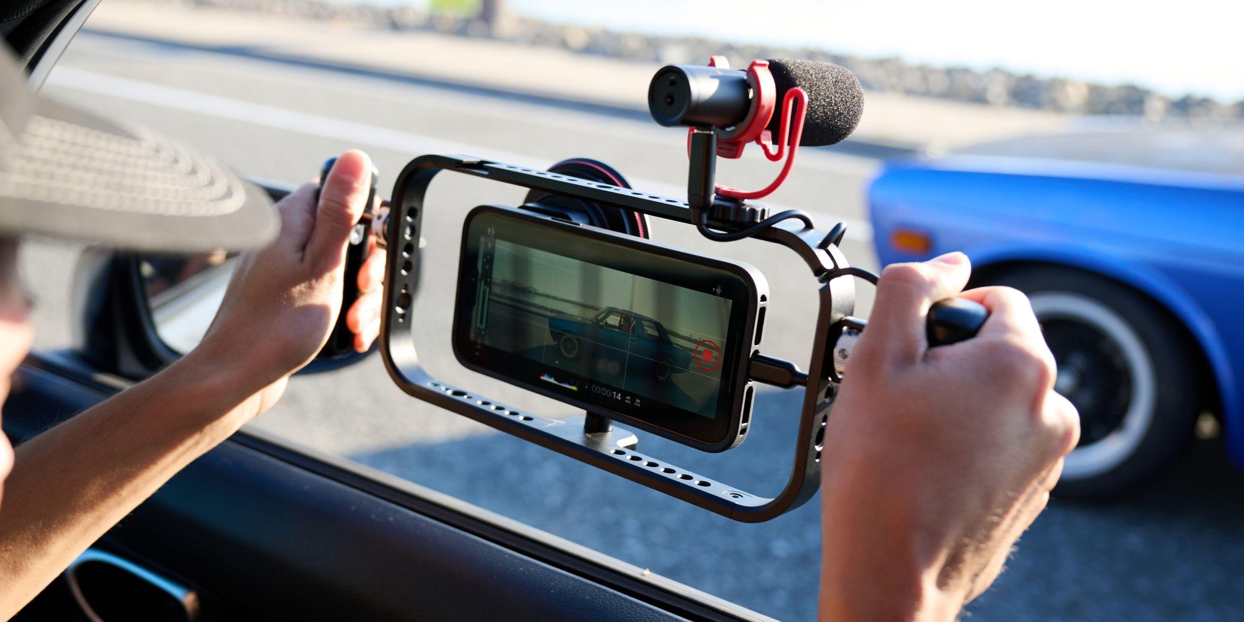 Hand holding iPhone 16 with a mobile filmmaker cage with an on-camera shotgun microphone for footage.